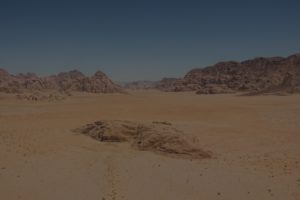 A desert with mountains in the background and sand.